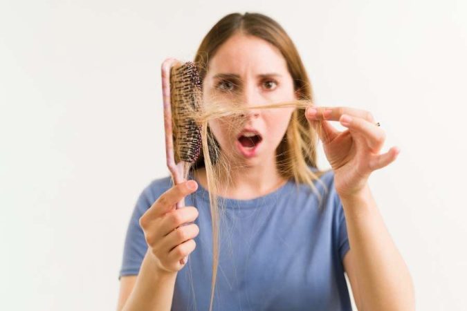 Femme choquée tenant une brosse remplie de cheveux abîmés et cassants