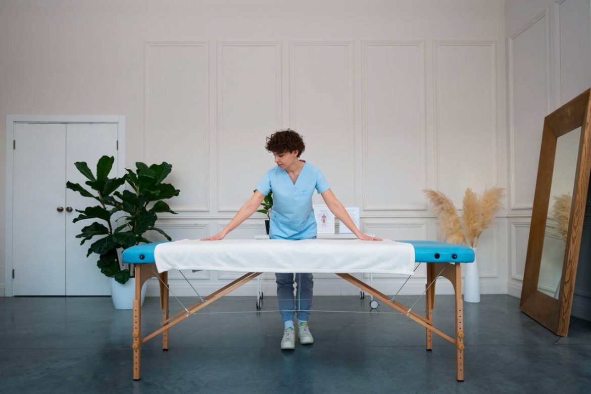 Praticienne installant une housse de protection propre pour entretenir une table de massage pliante professionnelle en bois dans son cabinet.