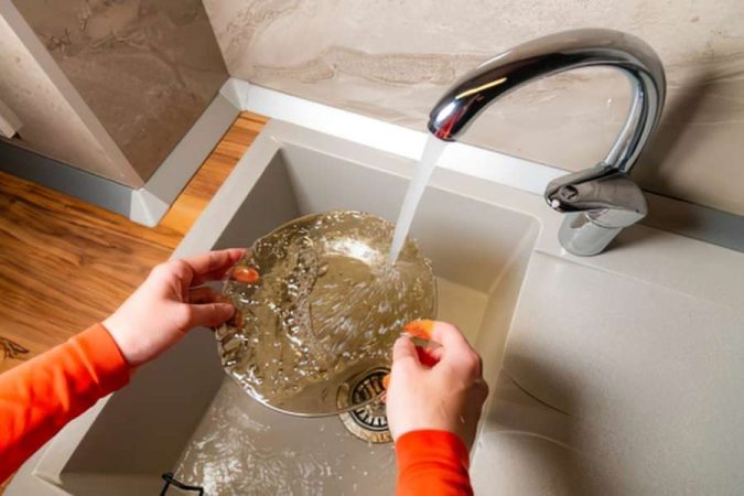 Une personne lave une assiette sous le robinet d'un évier moderne, ce qui peut encrasser la canalisation d'évier graisseuse.